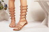 Femme portant des sandales gladiateur brun face montantes au genou avec brides à boucles, style punk romain, Zalmyraboutique.